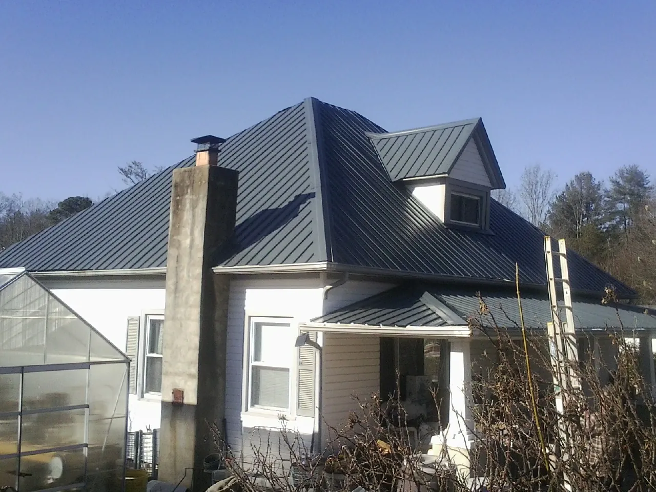Dark blue standing seam metal roof on a white farmhouse with dormer — Slate & Tile Roof Repair by Roofing Brothers in Powder Springs