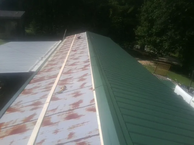 Old rusted panels beside newly installed green metal roofing — Wind Damage Roof Repair by Roofing Brothers in Powder Springs