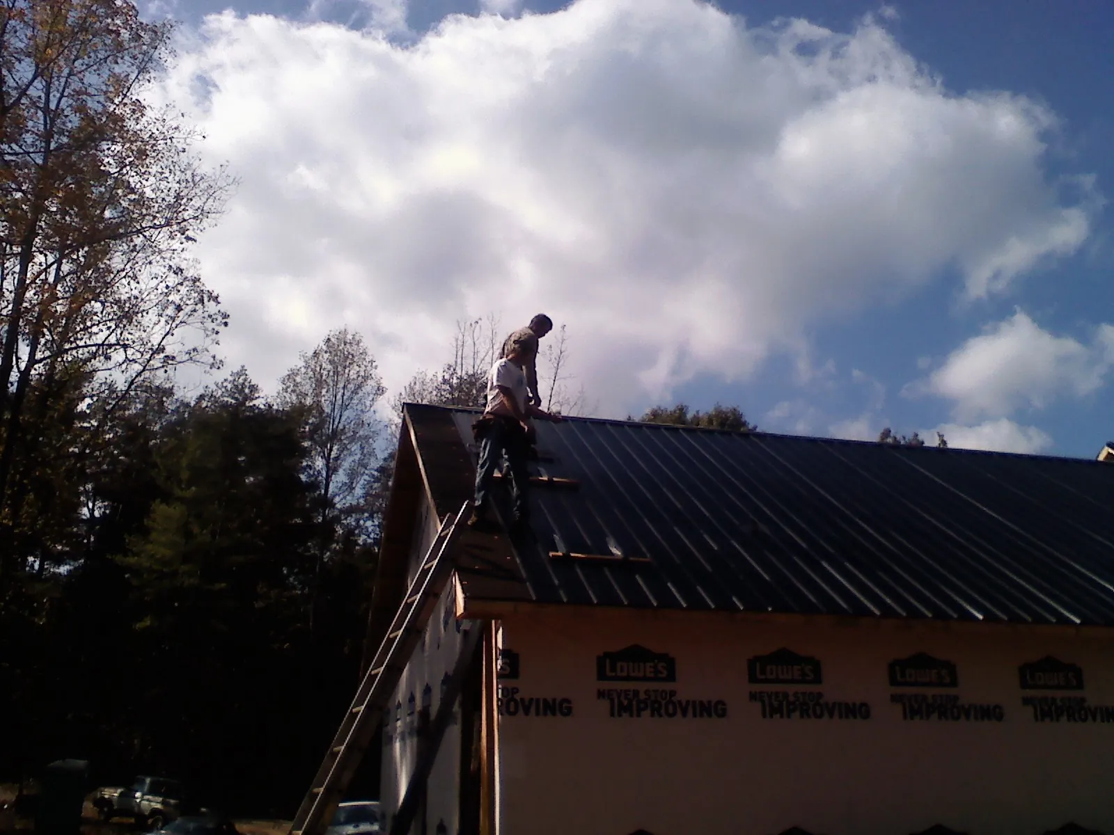Roofer fastening dark metal panels high against a cloudy sky, from a Roof Inspection job in Powder Springs